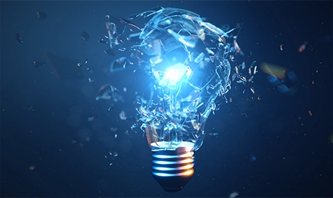 Shattered glass light bulb with glowing blue light at its center against a dark background.