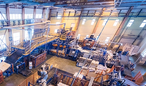 Interior view of a large manufacturing facility with industrial machinery, production lines, and equipment in operation.