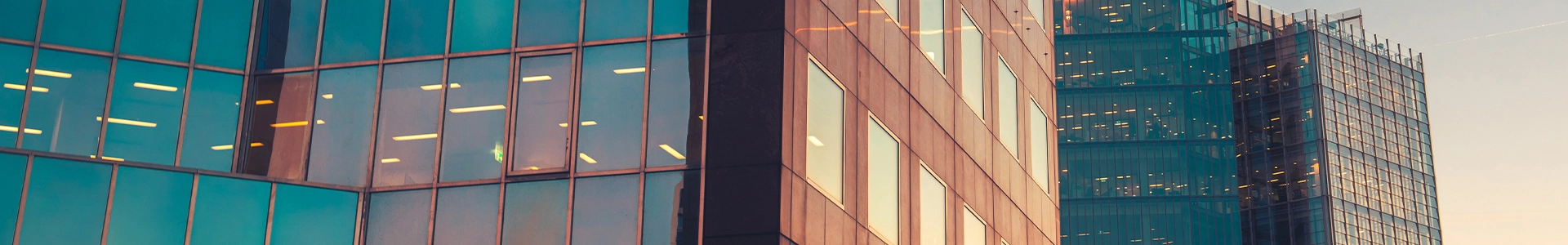 Modern glass office buildings reflecting a colorful sunset sky, showcasing contemporary urban architecture in a city skyline.