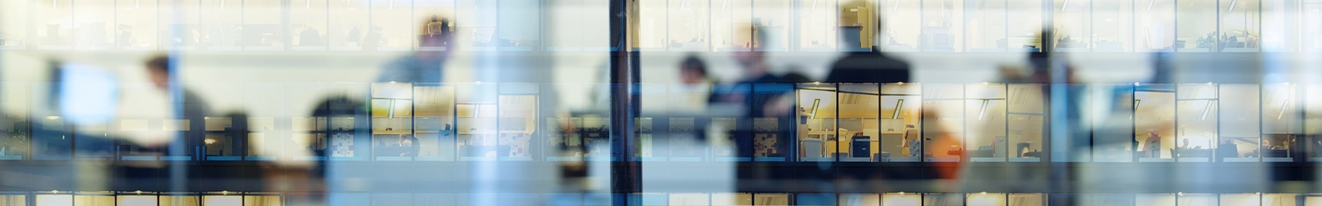 Blurred reflections of people working inside a multi‑story office building seen through large glass windows.