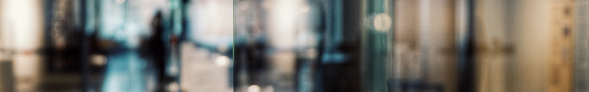 Abstract, blurred view of a modern office hallway with glass walls and soft ambient lighting.