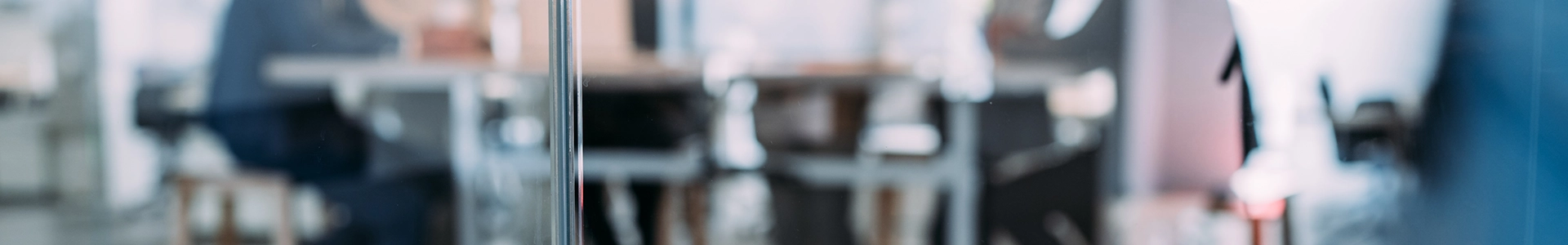 Blurred view of people working and meeting in a modern office behind a glass partition.