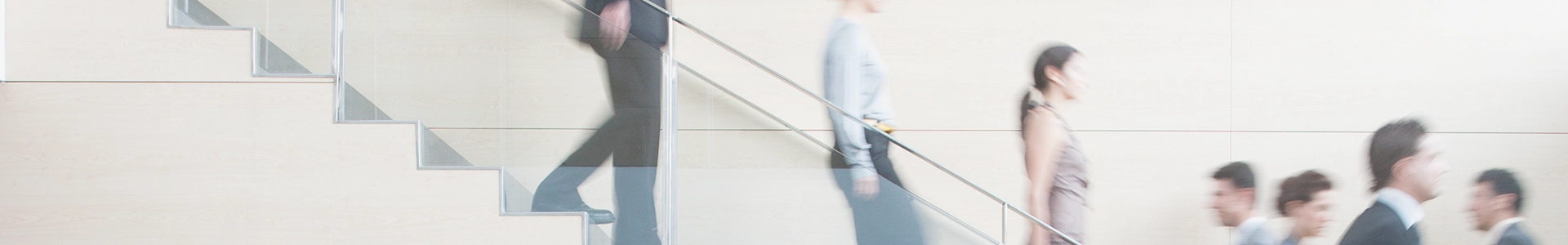 People walking up and down a modern indoor staircase, captured with motion blur against a light-colored wall.