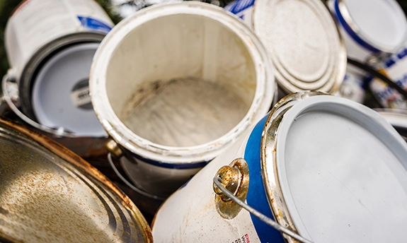 Pile of used and partially opened paint cans with worn lids and visible residue inside.
