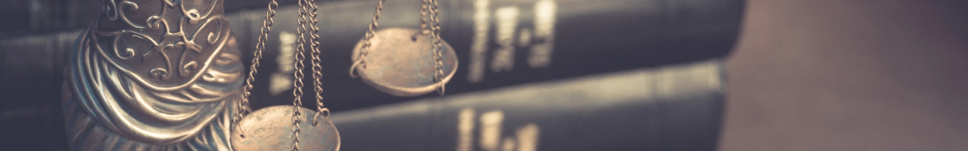 Close-up of a bronze statue holding scales in front of a stack of law books.