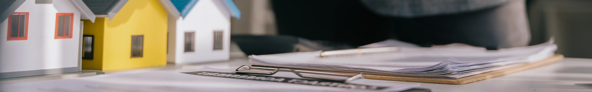 Small model houses next to a stack of documents on a clipboard on a desk.
