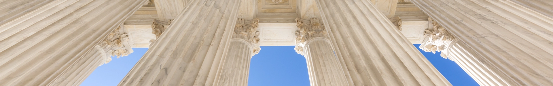 Upward view of large marble columns on a classical government-style building against a clear blue sky.