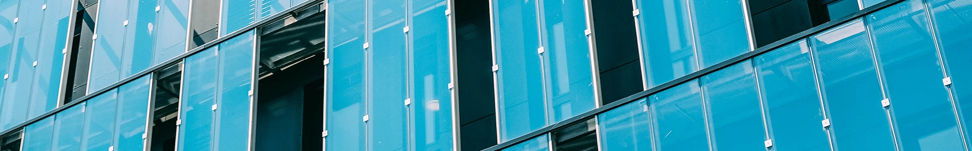 Close‑up view of modern glass office building exterior with blue panels and reflective windows.