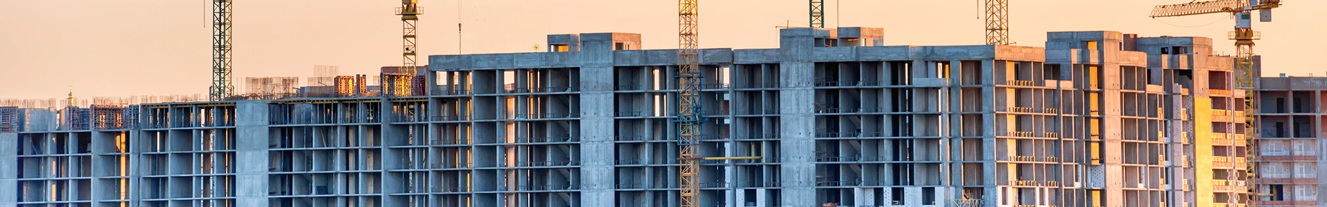 High-rise building under construction with multiple tower cranes operating at sunset.