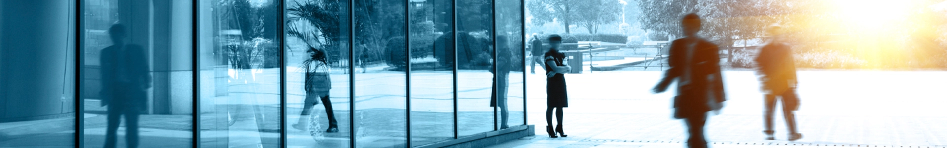 Business professionals walking near the glass entrance of a modern office building with cityscape reflections.