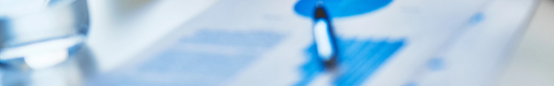 Blurred close-up of business documents with blue charts and a pen resting on top.