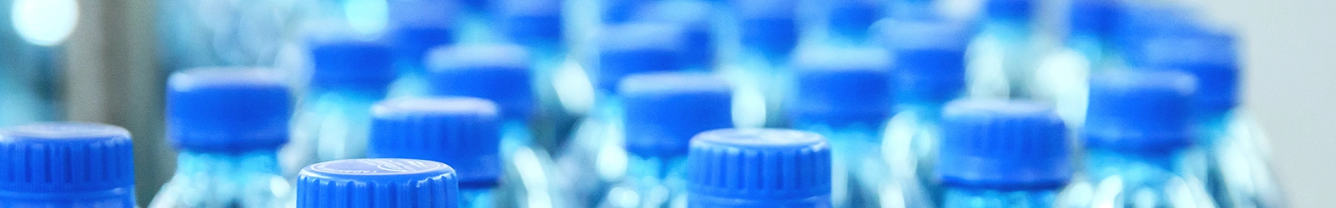 Rows of clear plastic water bottles with blue caps on a production line.