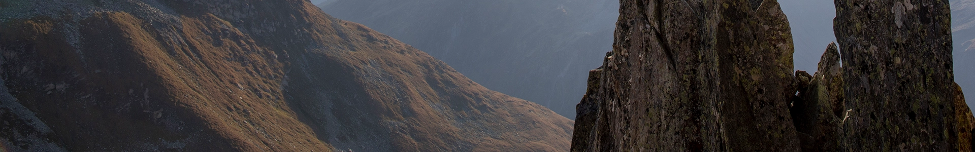 Mountain landscape with rugged rock formations in the foreground and steep, shadowed slopes in the background.