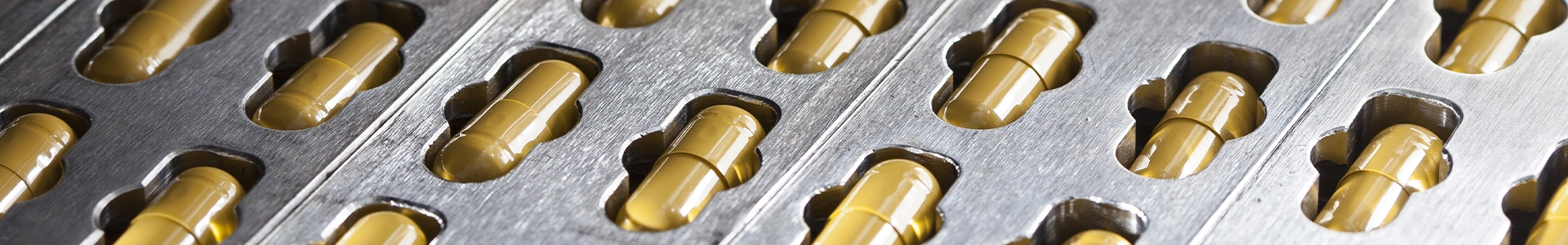 Close-up of a metal pharmaceutical manufacturing machine with rows of capsules in a production tray.