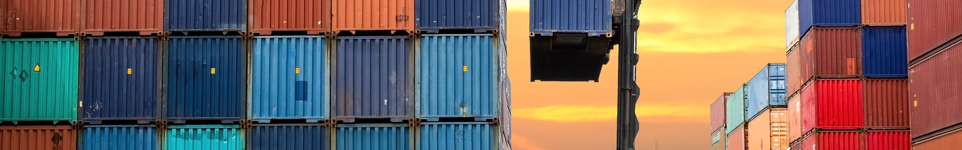 Stacked cargo containers in multiple colors at a shipping yard during sunset.