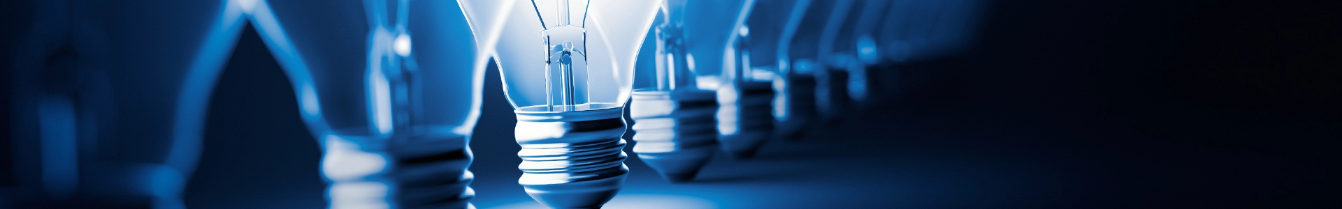 Row of light bulbs with one illuminated bulb glowing brightly against a dark background.