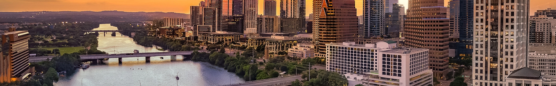 Panoramic view of the Austin skyline at sunset with high‑rise buildings along the river.