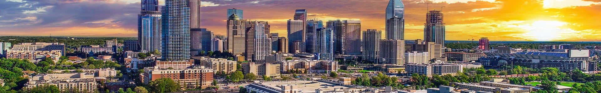 Panoramic view of the Charlotte skyline at sunset, showcasing vibrant city buildings and a colorful sky.