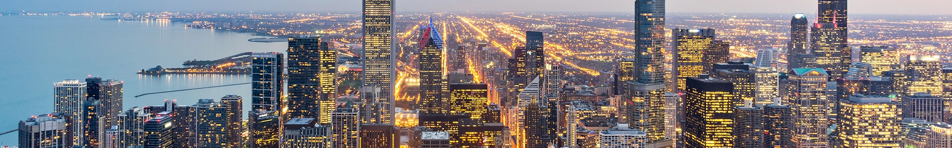 Panoramic view of the Chicago skyline at dusk featuring illuminated skyscrapers and Lake Michigan.