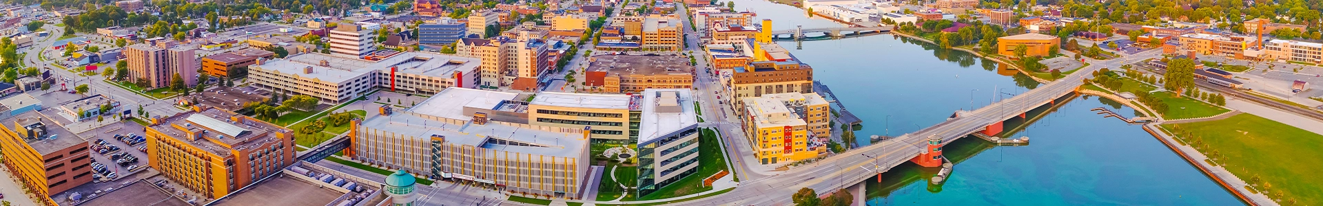 Panoramic aerial view of downtown Green Bay showcasing riverside buildings, bridges, and city architecture at sunrise.