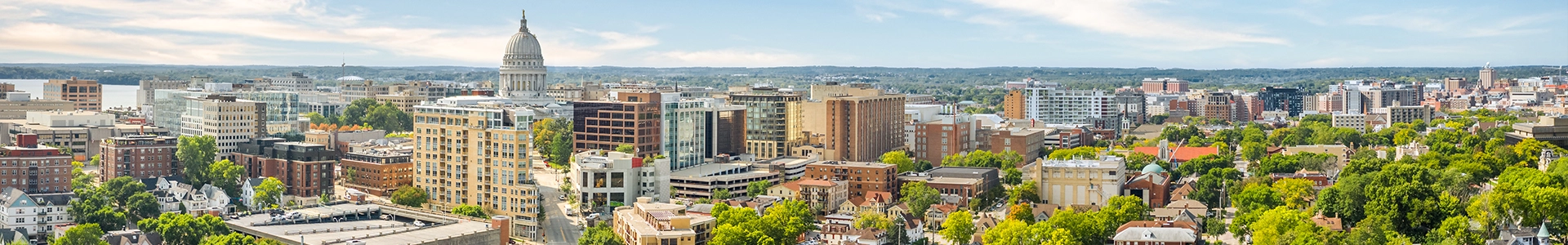 Panoramic view of downtown Madison featuring the Wisconsin State Capitol, surrounding buildings, and lush tree‑lined neighborhoods.