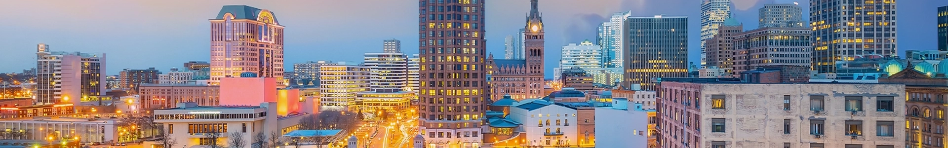 Panoramic view of downtown Milwaukee at dusk, featuring illuminated skyscrapers and historic buildings across the city skyline.