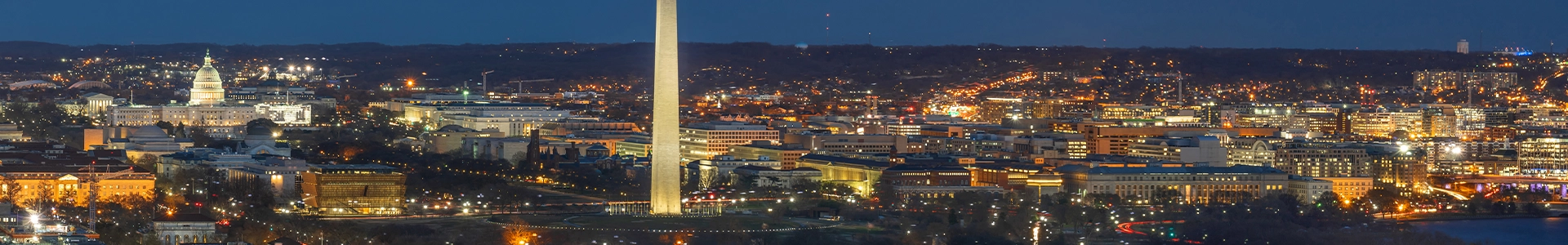 Panoramic nighttime view of Washington, D.C., featuring the Washington Monument, U.S. Capitol, and illuminated city skyline.