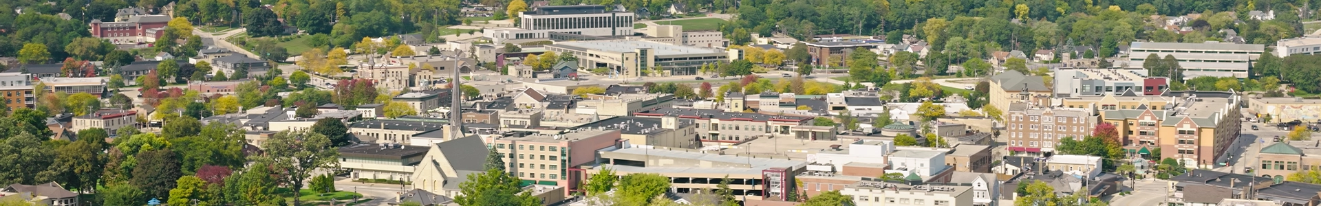 Aerial view of downtown Waukesha featuring city buildings, tree‑lined streets, and surrounding green neighborhoods.